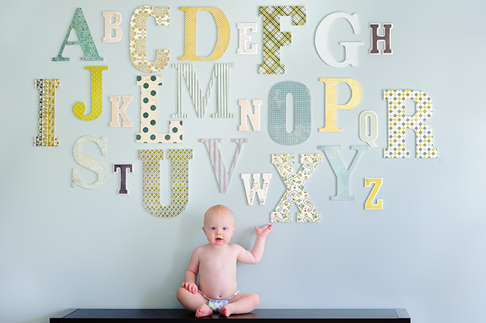A baby sitting in front of an alphabet wall, showcasing their personal branding.