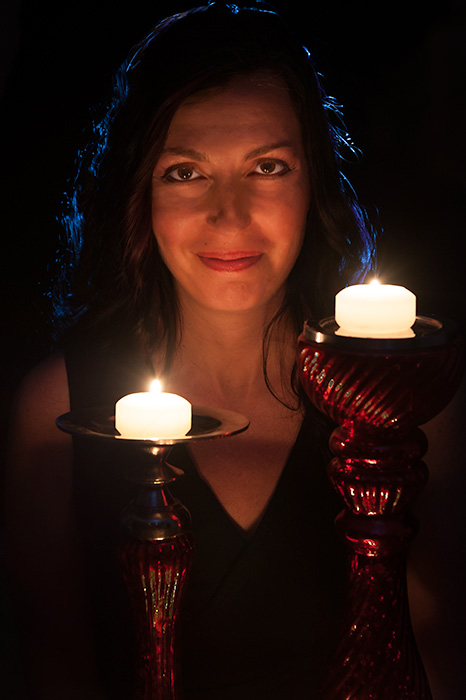 An elegantly dressed woman showcasing her personal branding talents, confidently holding two candles in front of a dark background.