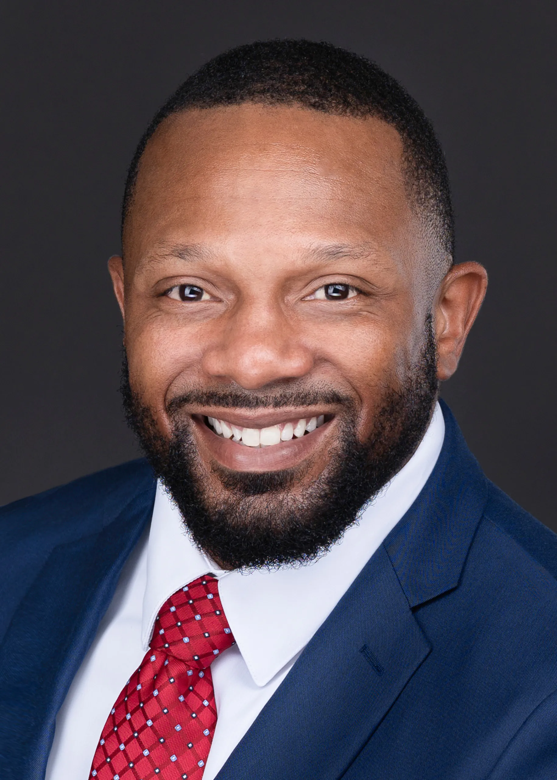 A professional photographer captures a an African American man in a suit and tie, smiling for an impressive corporate headshot.