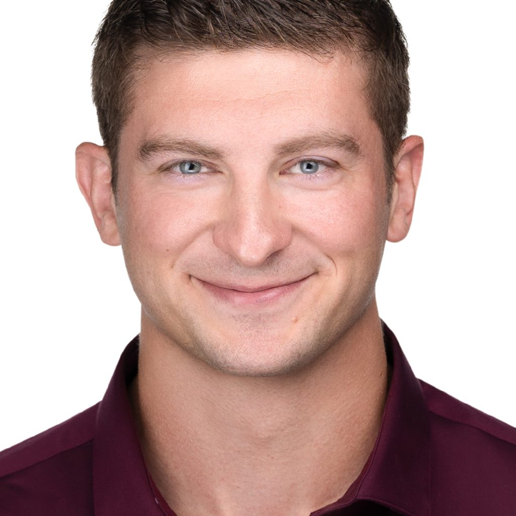 A man in a maroon shirt is smiling for his corporate headshot, showcasing his personal branding.