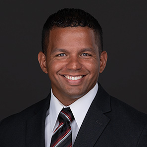 A military man transitioning from active duty to civilian life poses for a professional headshot wearing a suit and tie in front of a black backdrop in Cary NC