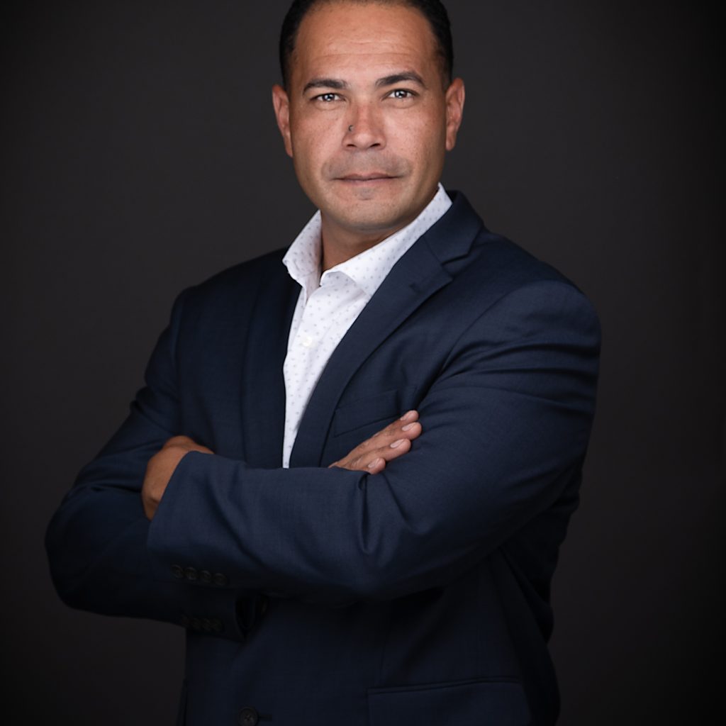 A man in a dark blue suit confidently poses for business headshots.