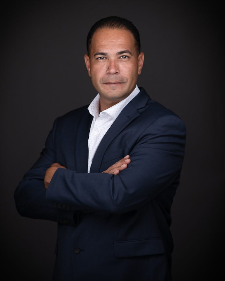 A man in a dark blue suit confidently poses for business headshots.