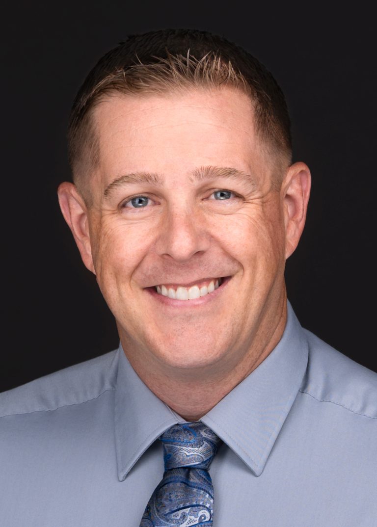 A man in a blue shirt and tie poses for professional headshots captured by a skilled photographer.