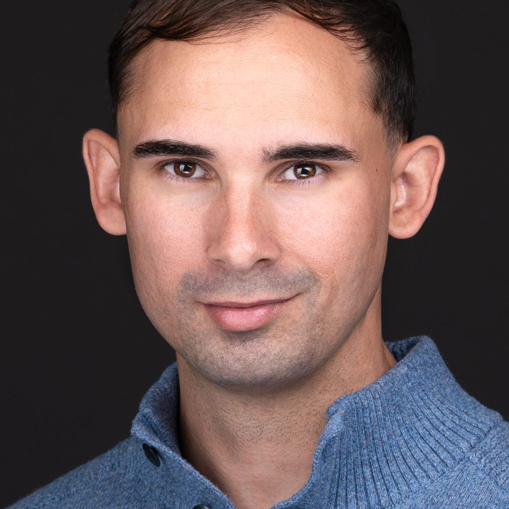 A professional headshot photographer captures a man with brown eyes wearing a blue henley sweater for his business headshot.