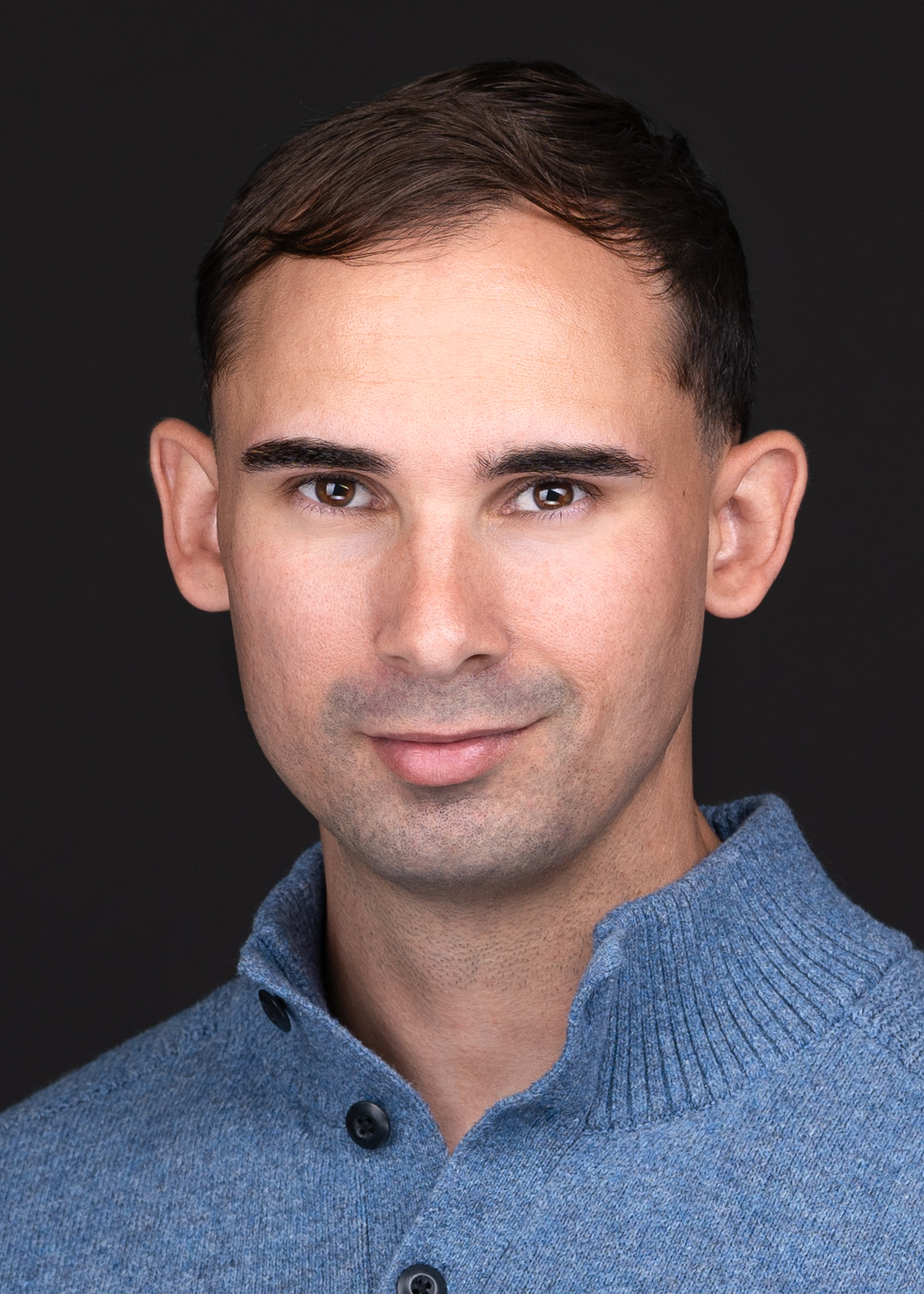 A professional headshot photographer captures a man with brown eyes wearing a blue henley sweater for his business headshot.