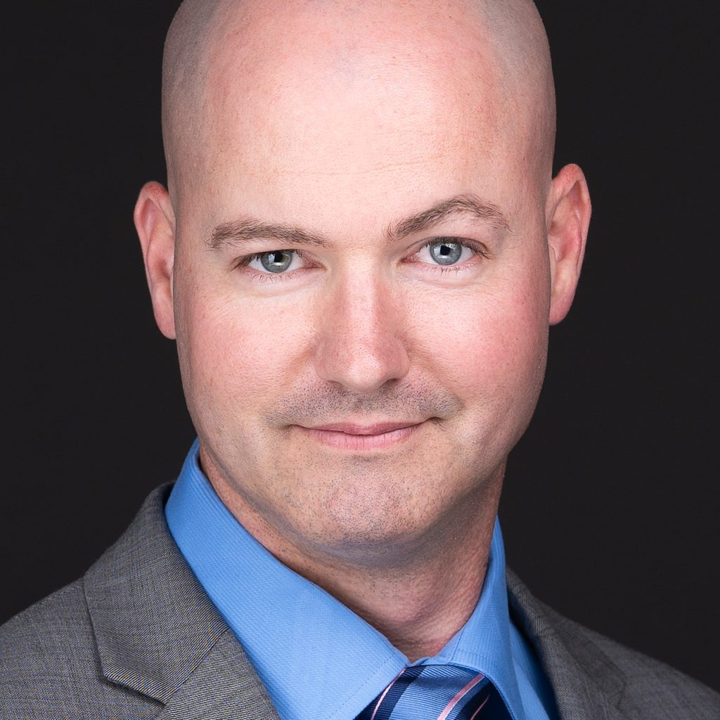 A professional headshot photographer in Raleigh NC captures a man with a single raised eyebrow in a grey suit and tie for corporate headshots.