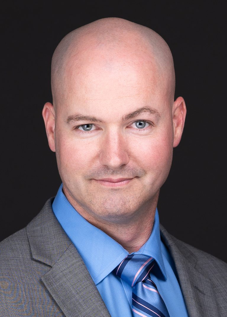 A professional headshot photographer in Raleigh NC captures a man with a single raised eyebrow in a grey suit and tie for corporate headshots.