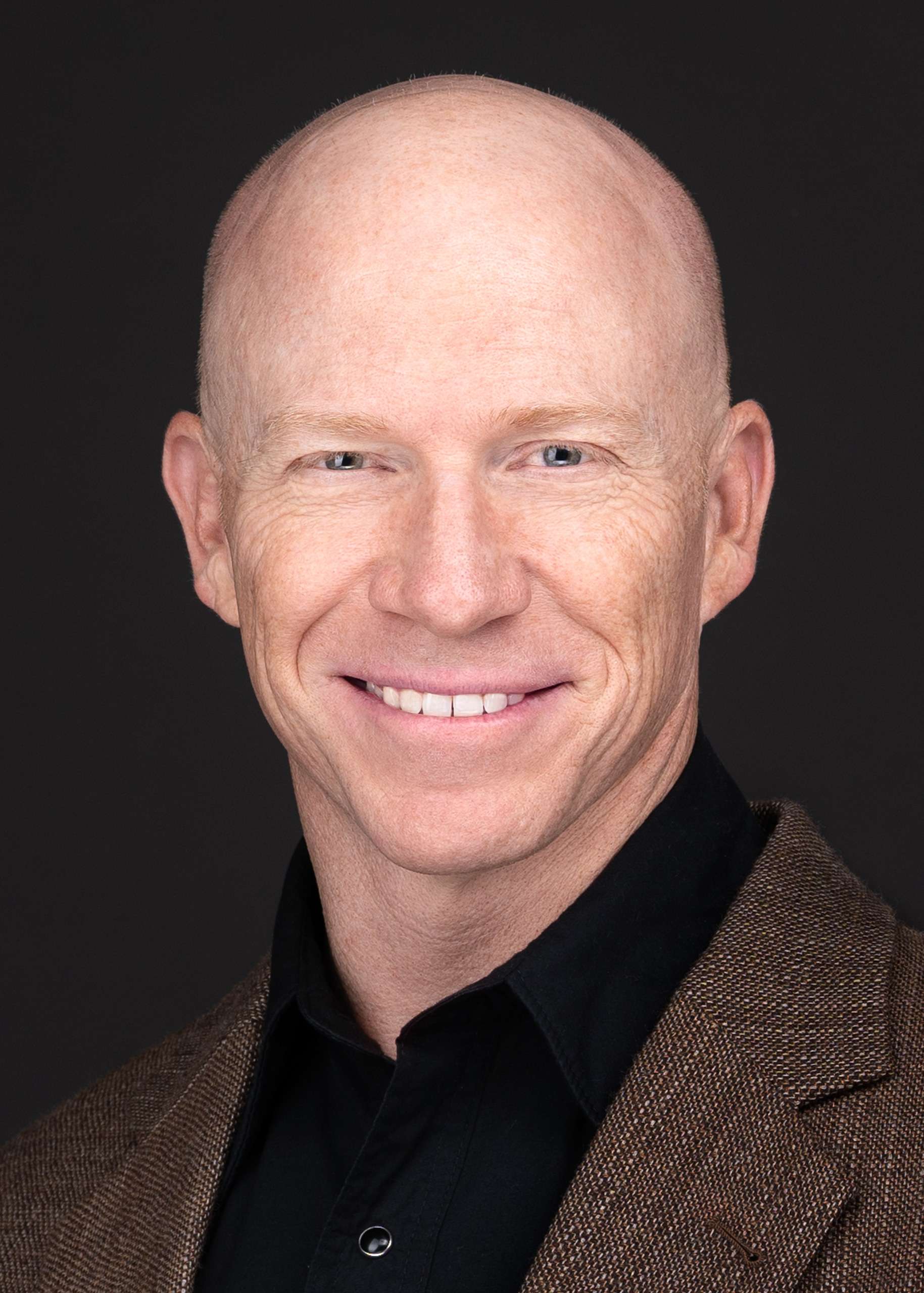 A bald man with a genuine smile poses for a business headshot captured by Sarah Anne Wilson Photography in Cary, North Carolina.