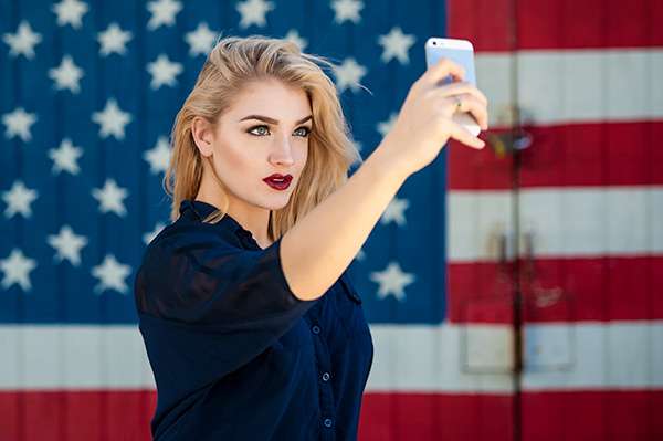 An actress holds a cell phone and poses in front of a wall, painted with the American flag for personal branding photos in Raleigh NC