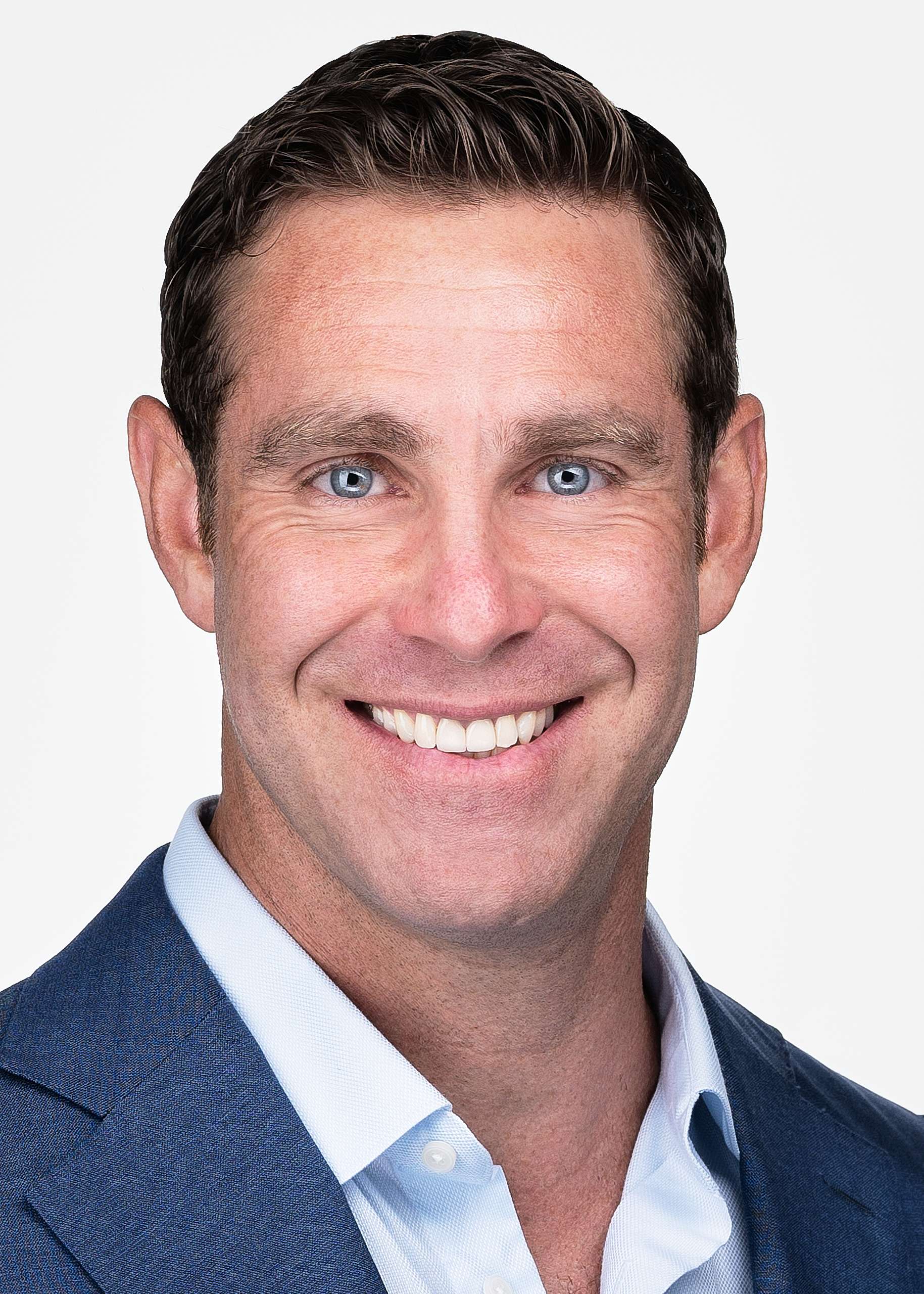 A man with a blue suit poses for a professional headshot against a white backdrop in Cary NC