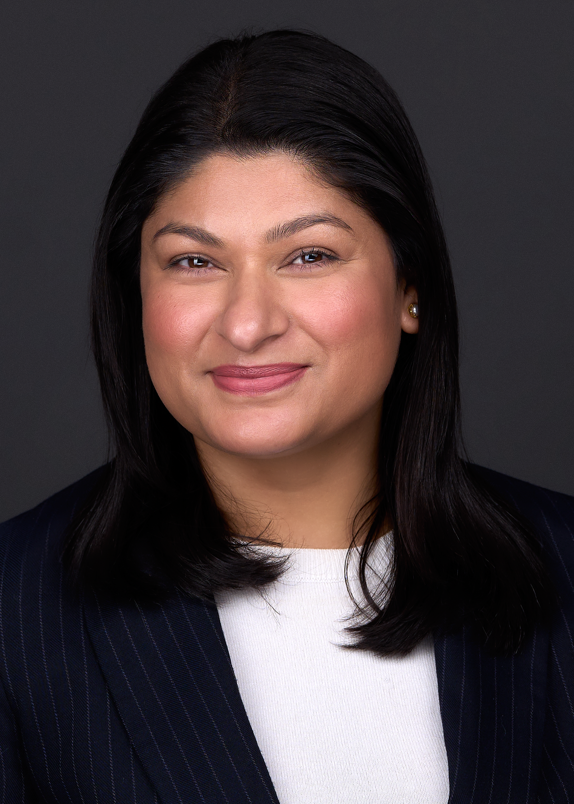 A Hispanic women with black hair wears a blue suit while sitting for a professional headshot in Raleigh NC