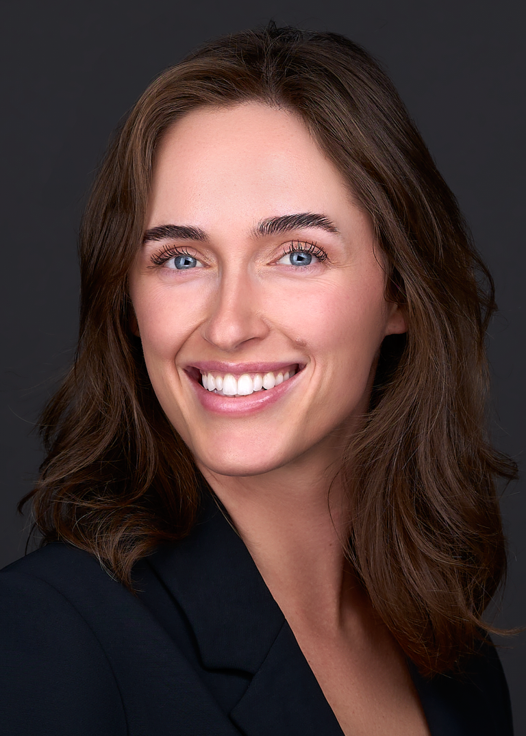 A business women stands for a professional headshot in front of a black backdrop while wearing a blue suit. She poses for this headshot in a photography studio in Cary NC