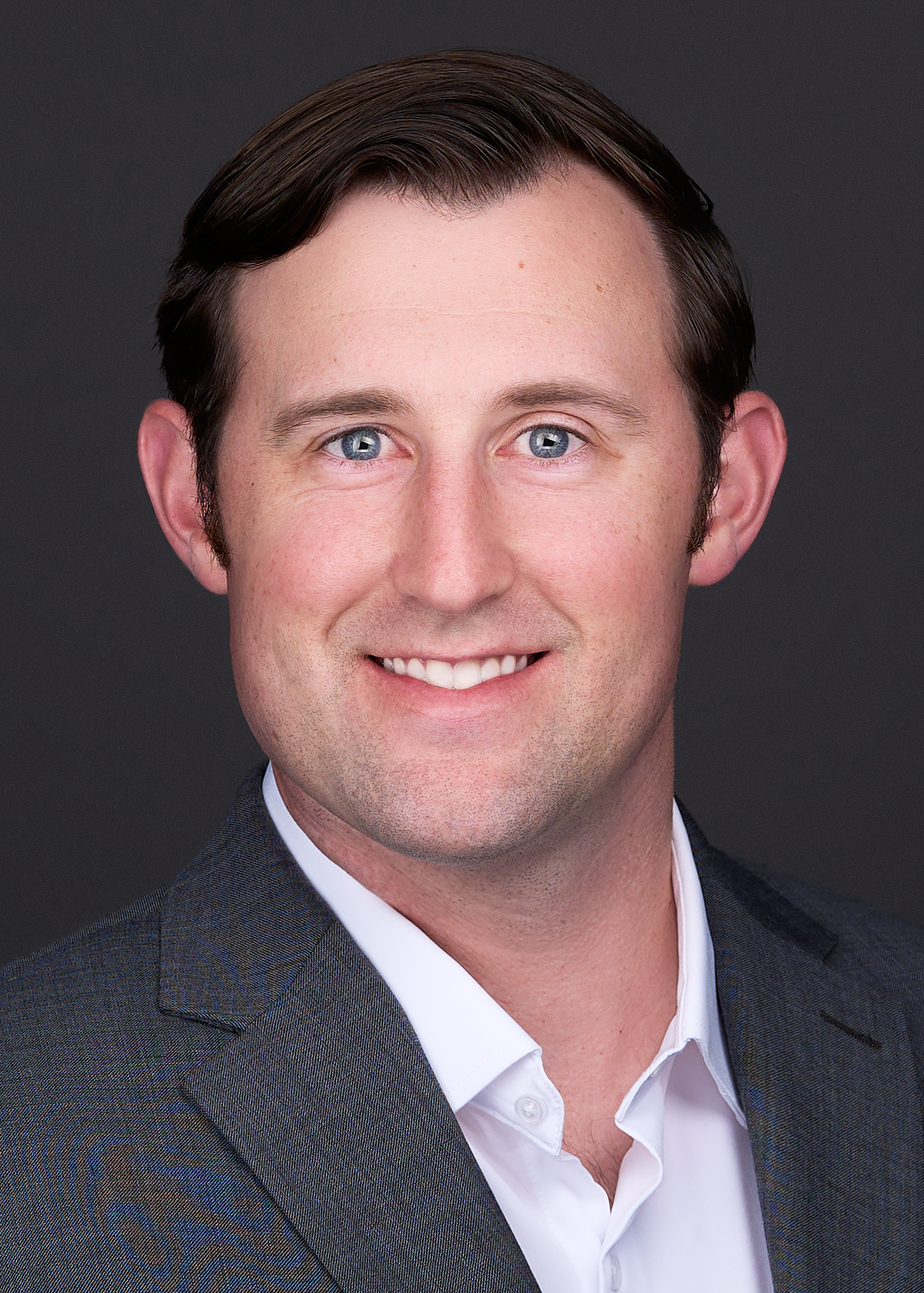 A Patriot poses for a professional headshot session wearing a grey suit and white shirt.