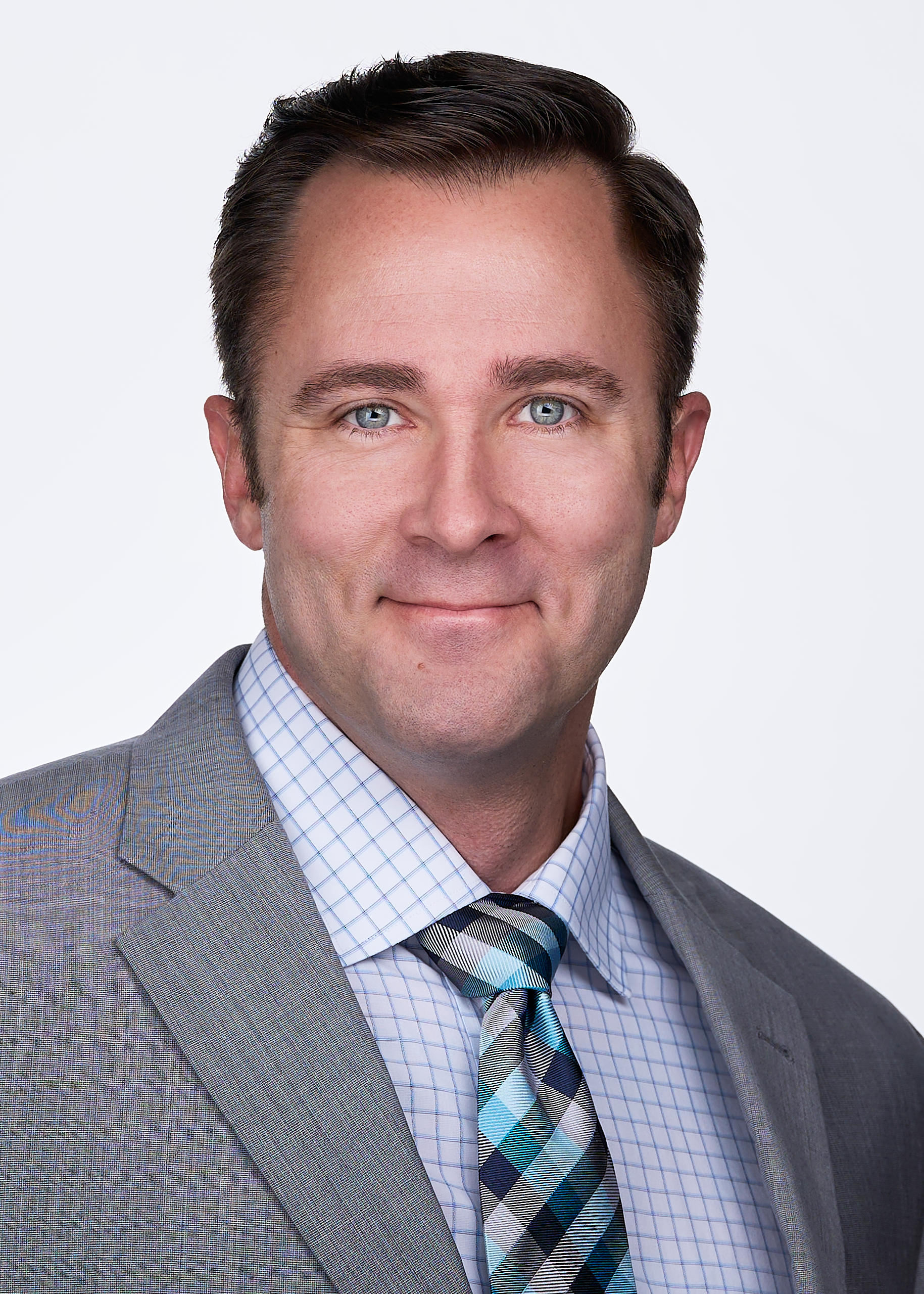 A business professional poses for a headshot wearing a grey suit, plaid tie and striped shirt in a photography studio in Raleigh NC