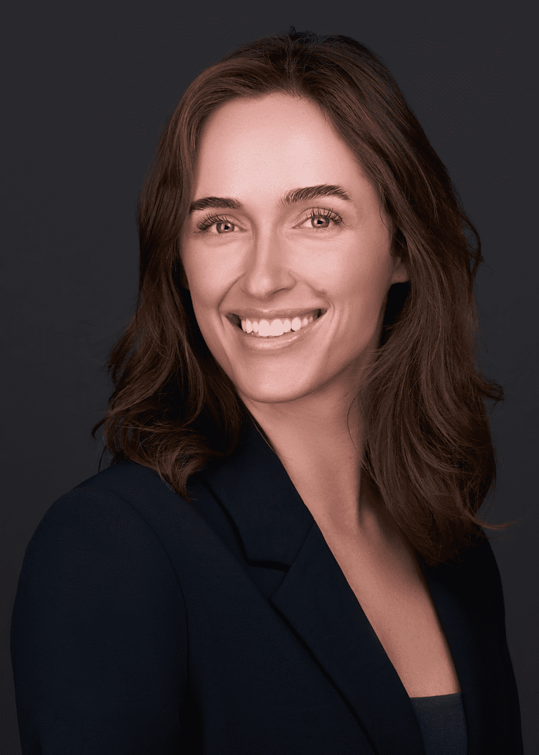 A business women stands for a professional headshot in front of a black backdrop while wearing a blue suit. She poses for this headshot in a photography studio in Cary NC