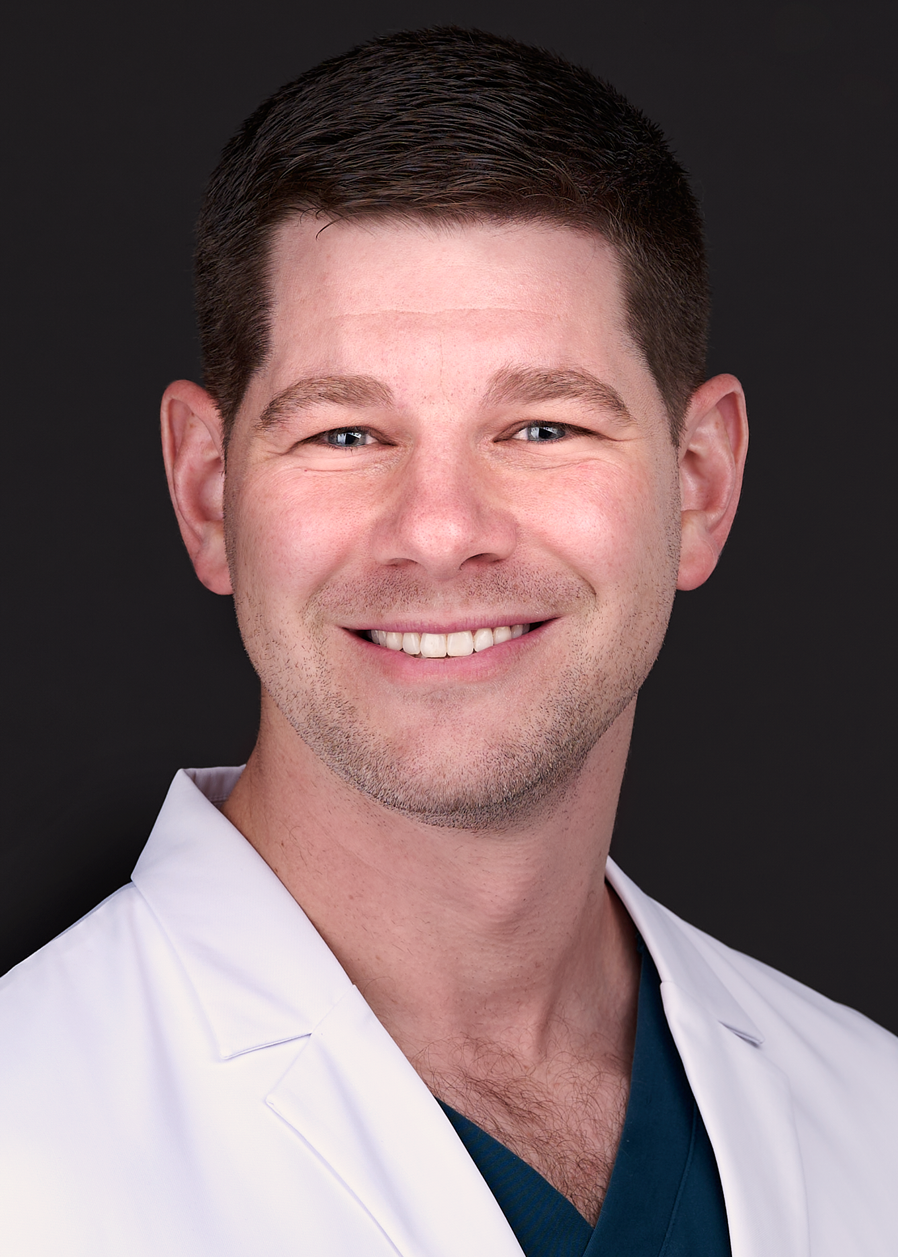 A Chiropractor poses for a professional headshot wearing dark teal scrubs and a white medical coat in Raleigh NC