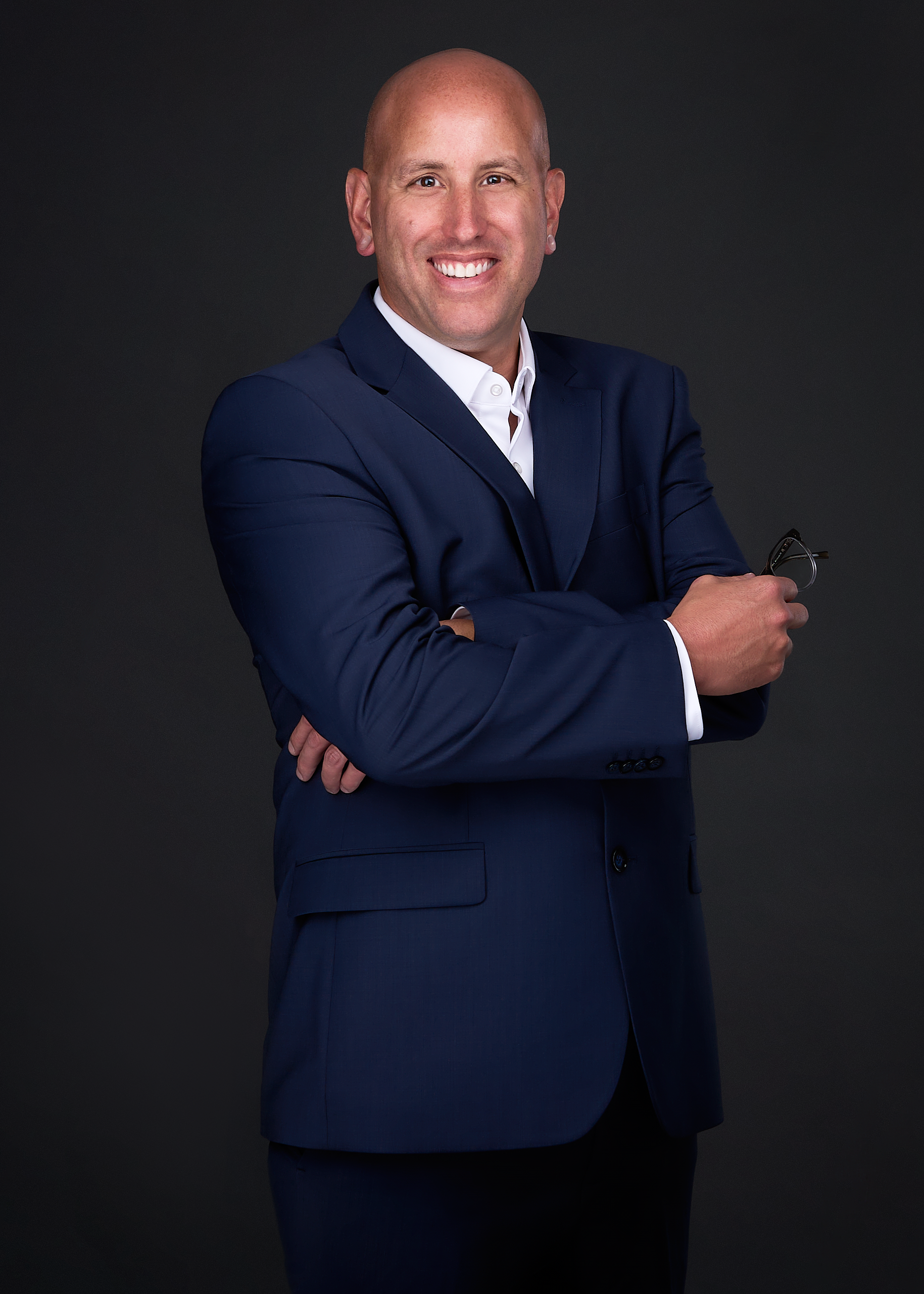 A man poses for a personal branding image wearing a blue suit and holding a pair of glasses in the photography studio of Sarah Anne Wilson