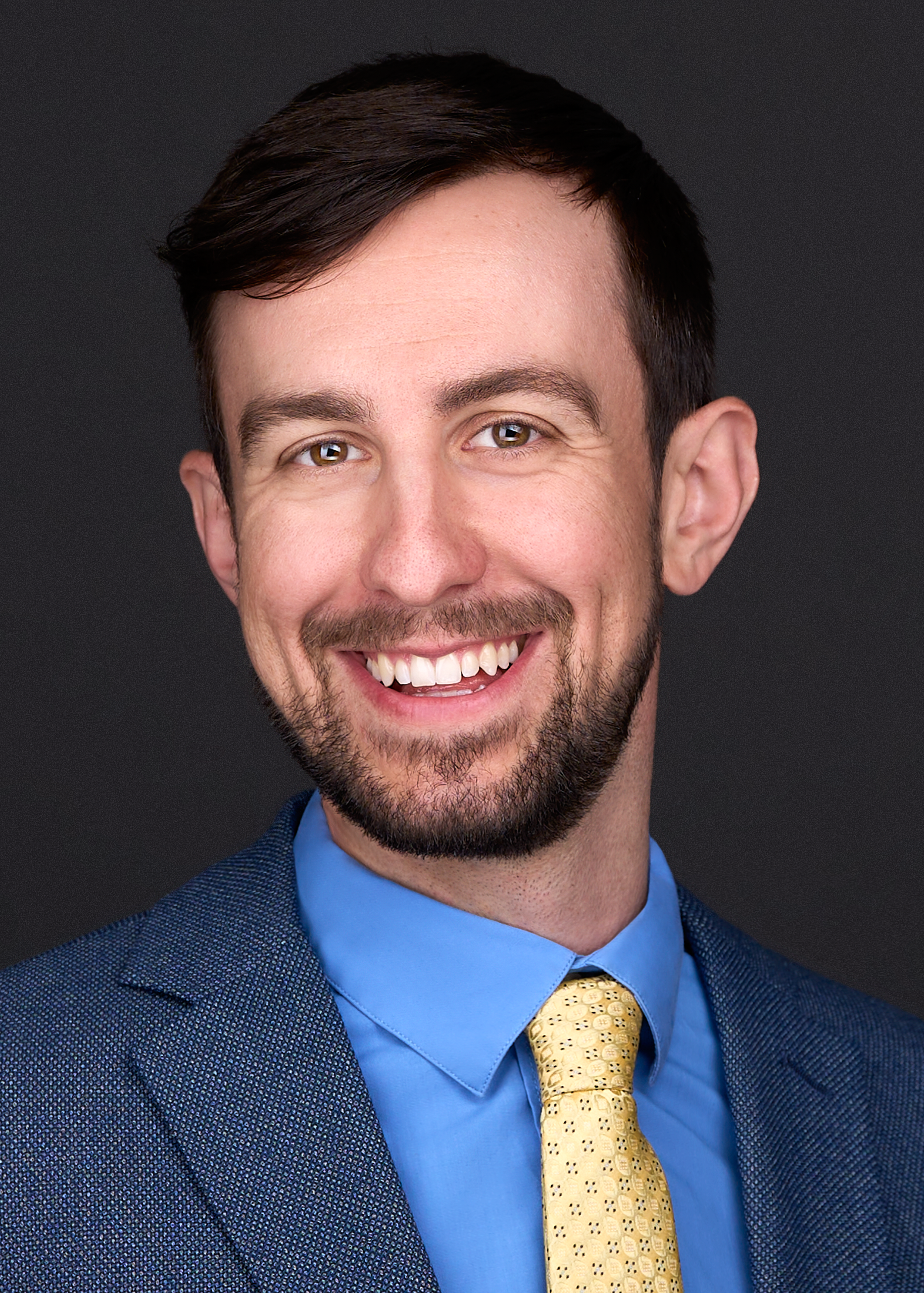 A doctor poses for a personal branding image wearing a blue suit and bright yellow tie at a photography studio in Raleigh NC