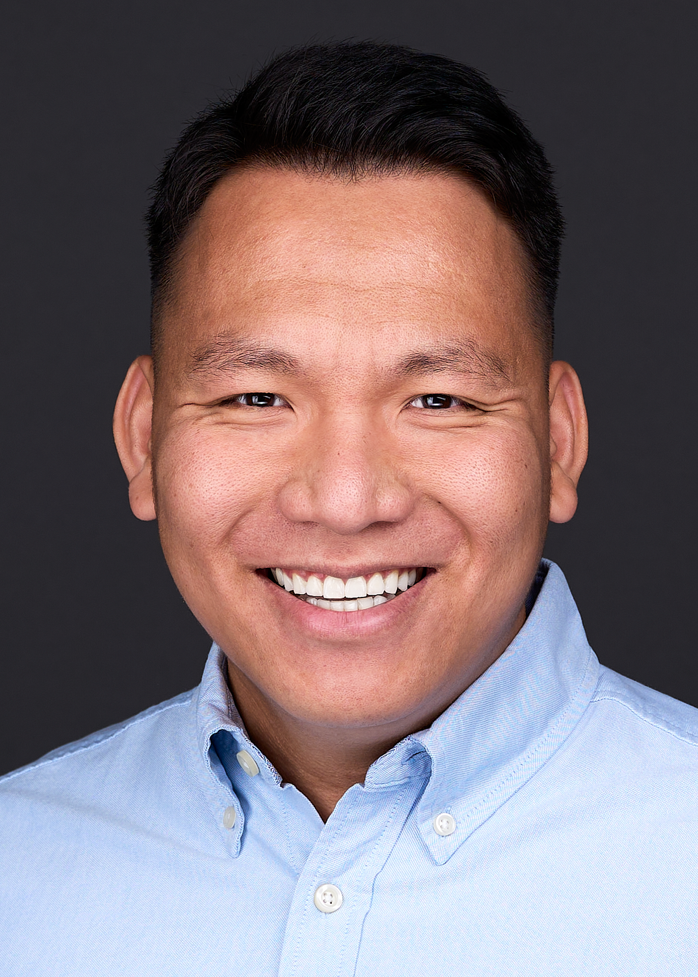 A Headshot Photographer creates an image of an Asian man wearing a blue dress shirt in a portrait studio in Cary NC