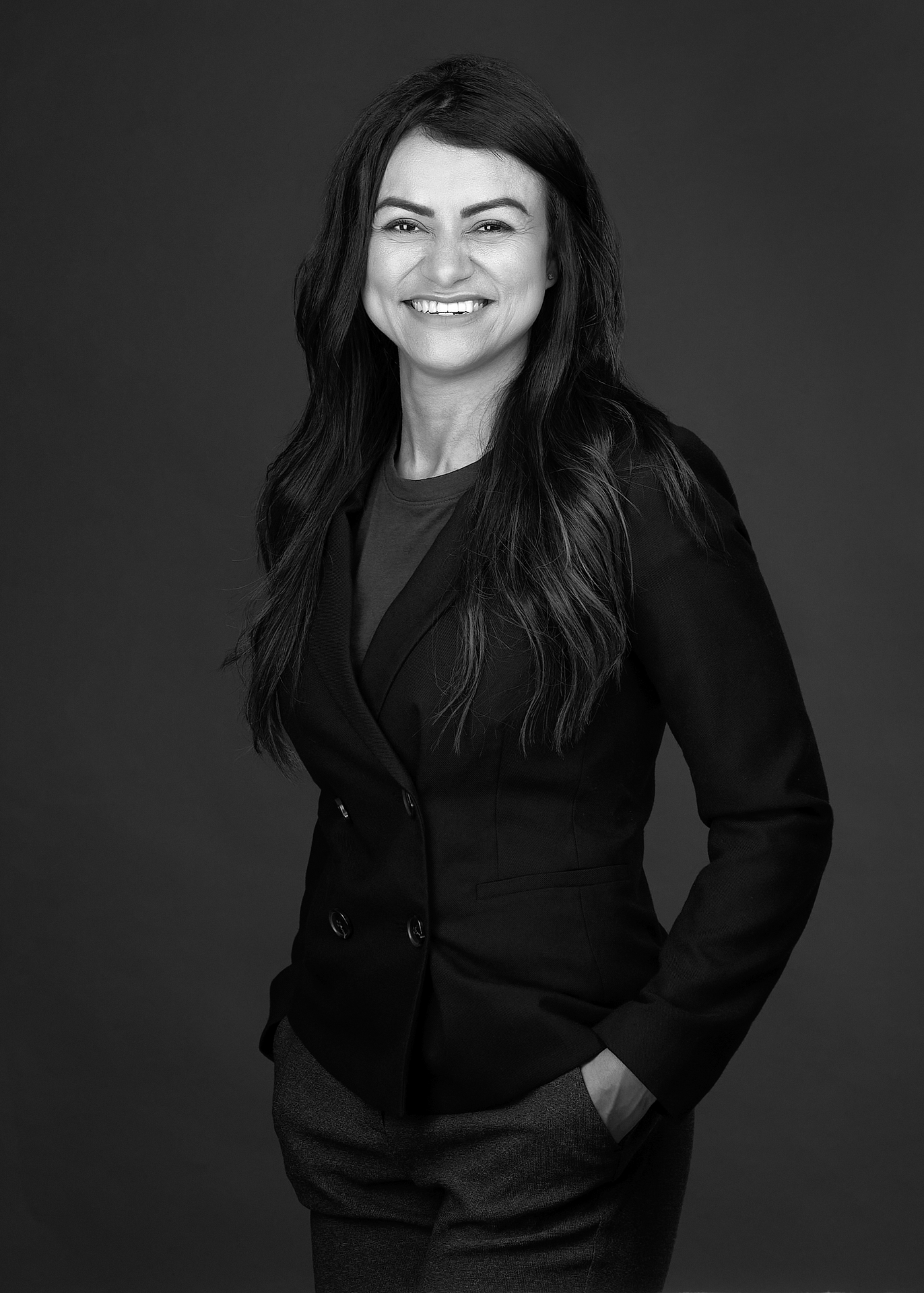 A young woman with her hands in her pockets poses for a black and white personal branding image in a photography studio