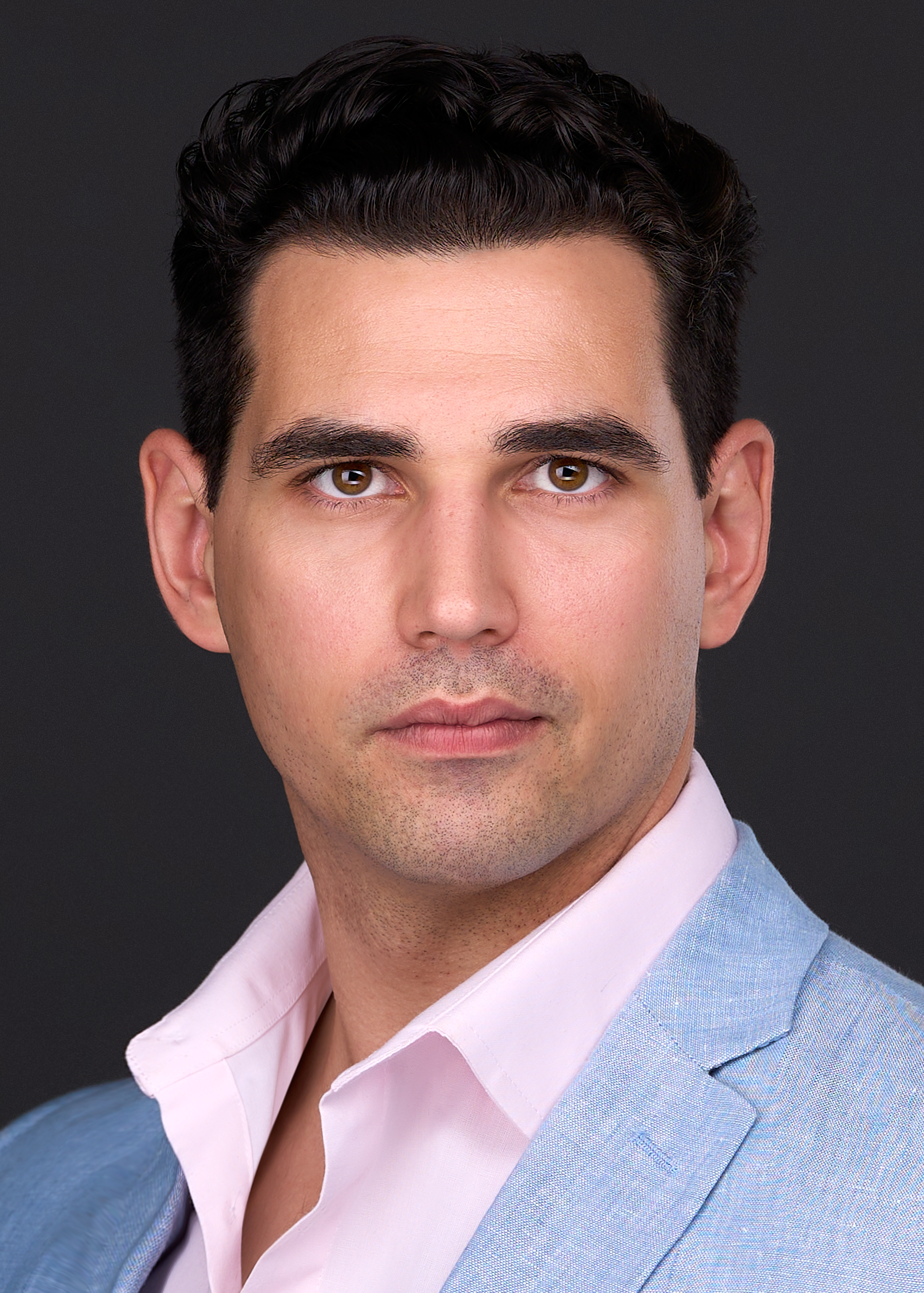 A man in a light blue suit and pink shirt models for a professional headshot in Cary Nc