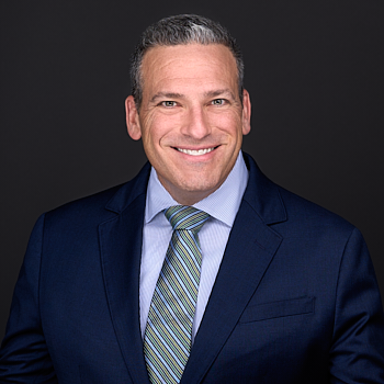 A man wearing blue suit and striped tie smiles as he poses for a lawyers headshot in Cary NC