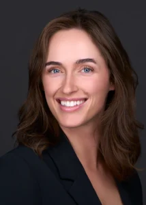 A business women stands for a professional headshot in front of a black backdrop while wearing a blue suit. She poses for this headshot in a photography studio in Cary NC