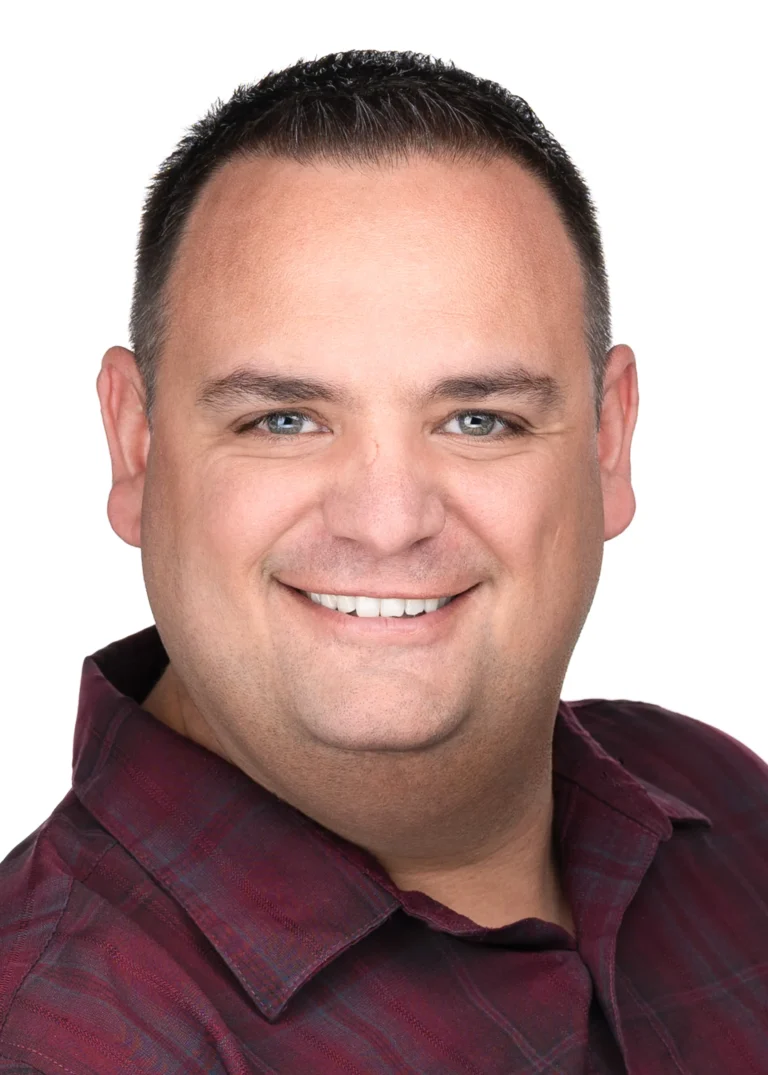 Smiling man with short dark hair wearing a maroon plaid shirt, photographed against a white background.