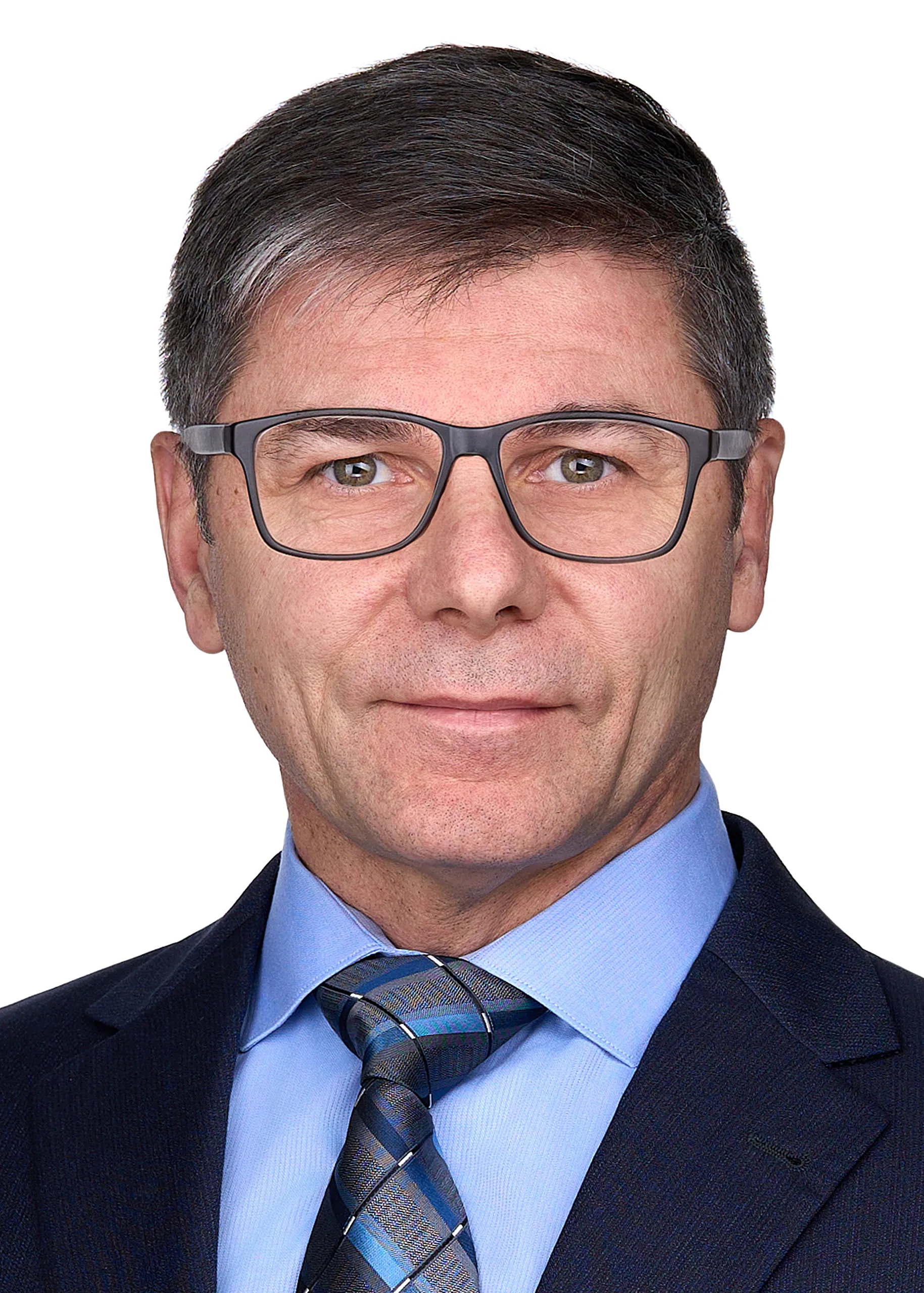 A man wearing glasses, a blue suit poses for a professional headshot with a serious expression in the photography studio of Sarah Anne Wilson Photography