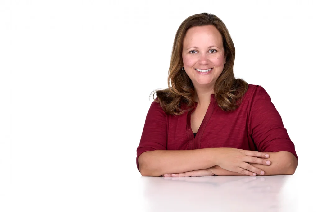 A woman with long brown hair wearing a red blouse leans on a table for a personal branding photo in a photography studio in Raleigh Nc