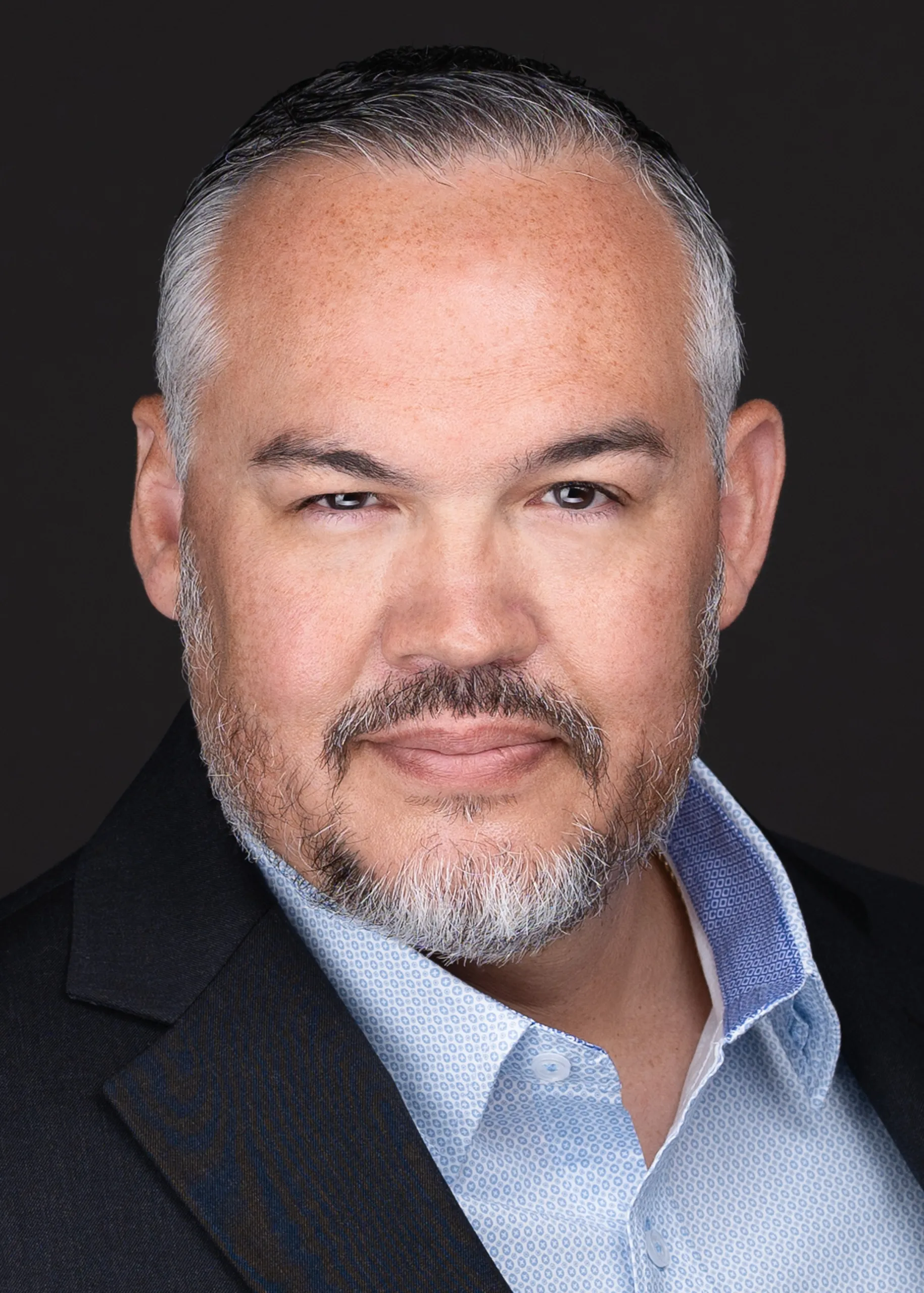 A man with a beard and a blue shirt poses for corporate headshots in front of the camera of Sarah Anne Wilson Photography in Cary, North Carolina, showcasing his personal branding.