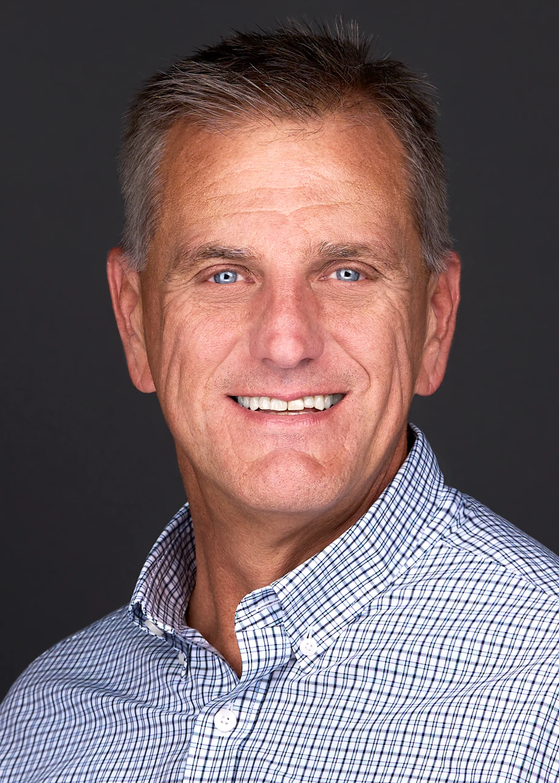 A man in a plaid shirt smiles for the camera as he poses for a professional headshot in Cary Nc