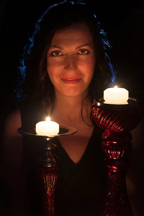 A woman with long black hair stands in front of two lit candles as she poses for a professional headshot in Raleigh Nc