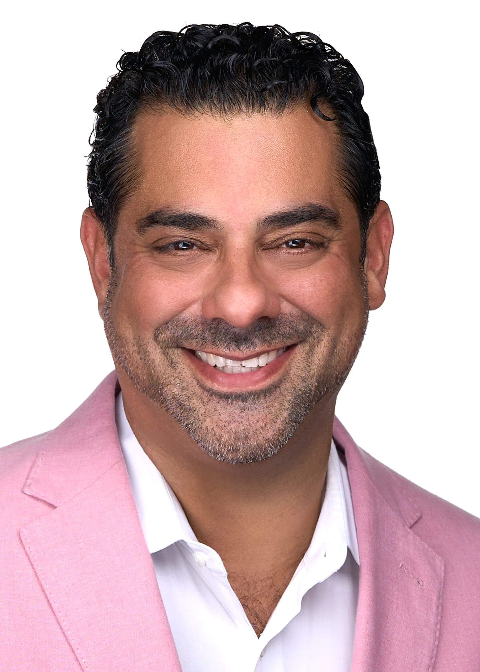 A man with black hair wears a pink blazer as he smiles for a professional headshot while standing in front of a white backdrop in Raleigh Nc