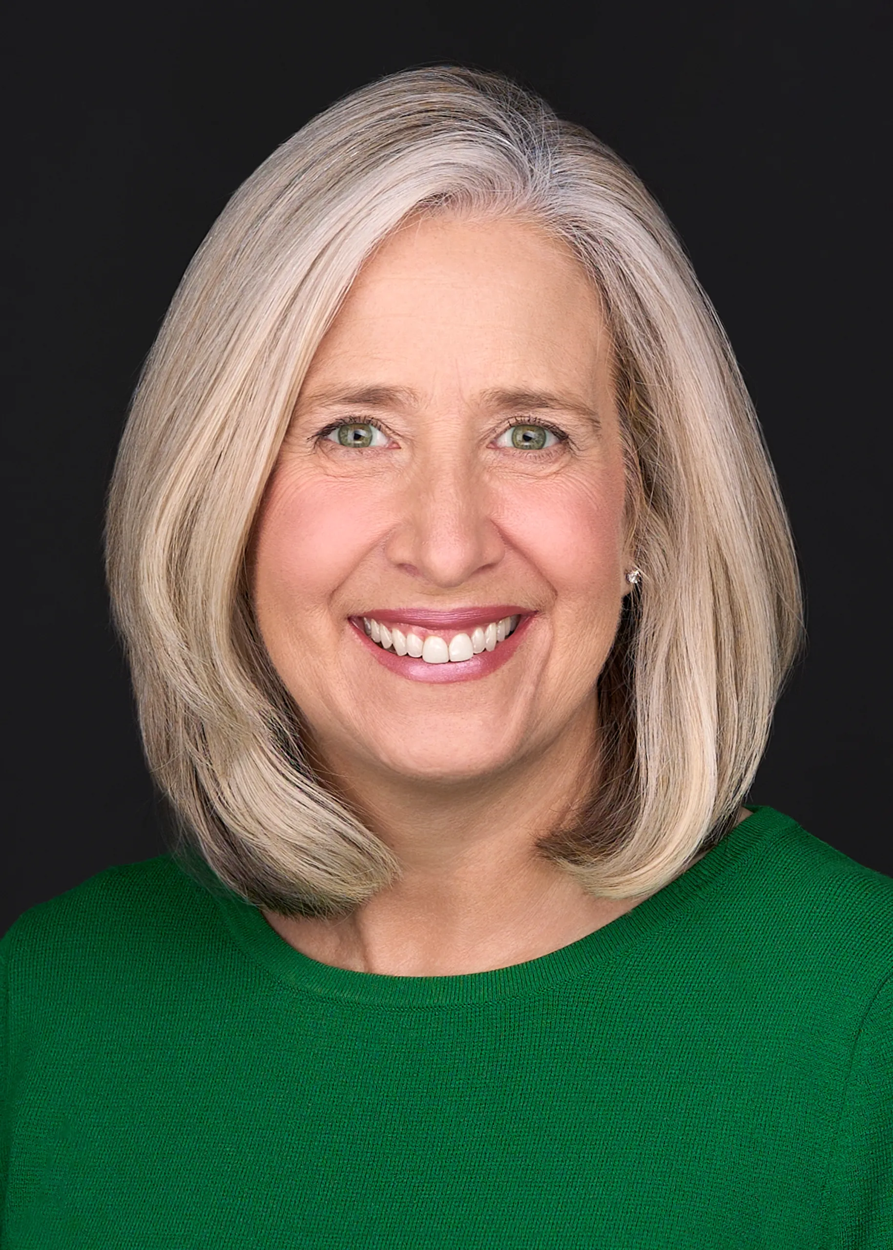 A women with gray hair and a bright green sweater smiles beautifully while posing for a professional headshot in front of a black background in Raleigh Nc