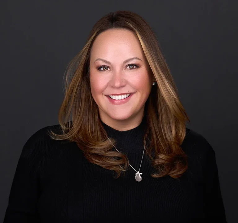 A young woman with long brown hair wearing a black turtleneck sweater stands for a personal branding photo while standing in front of a black backdrop