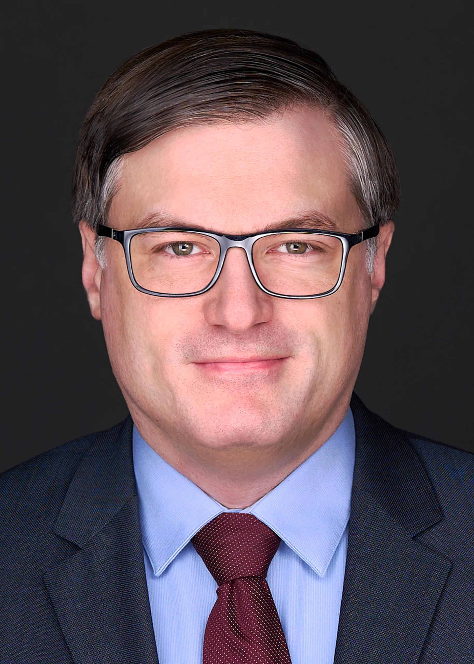 A middle aged man wearing glasses, a blue shirt and blue suit, smiles gently as he poses for a Lawyer headshot in the studio of Sarah Anne Wilson Photography Raleigh NC