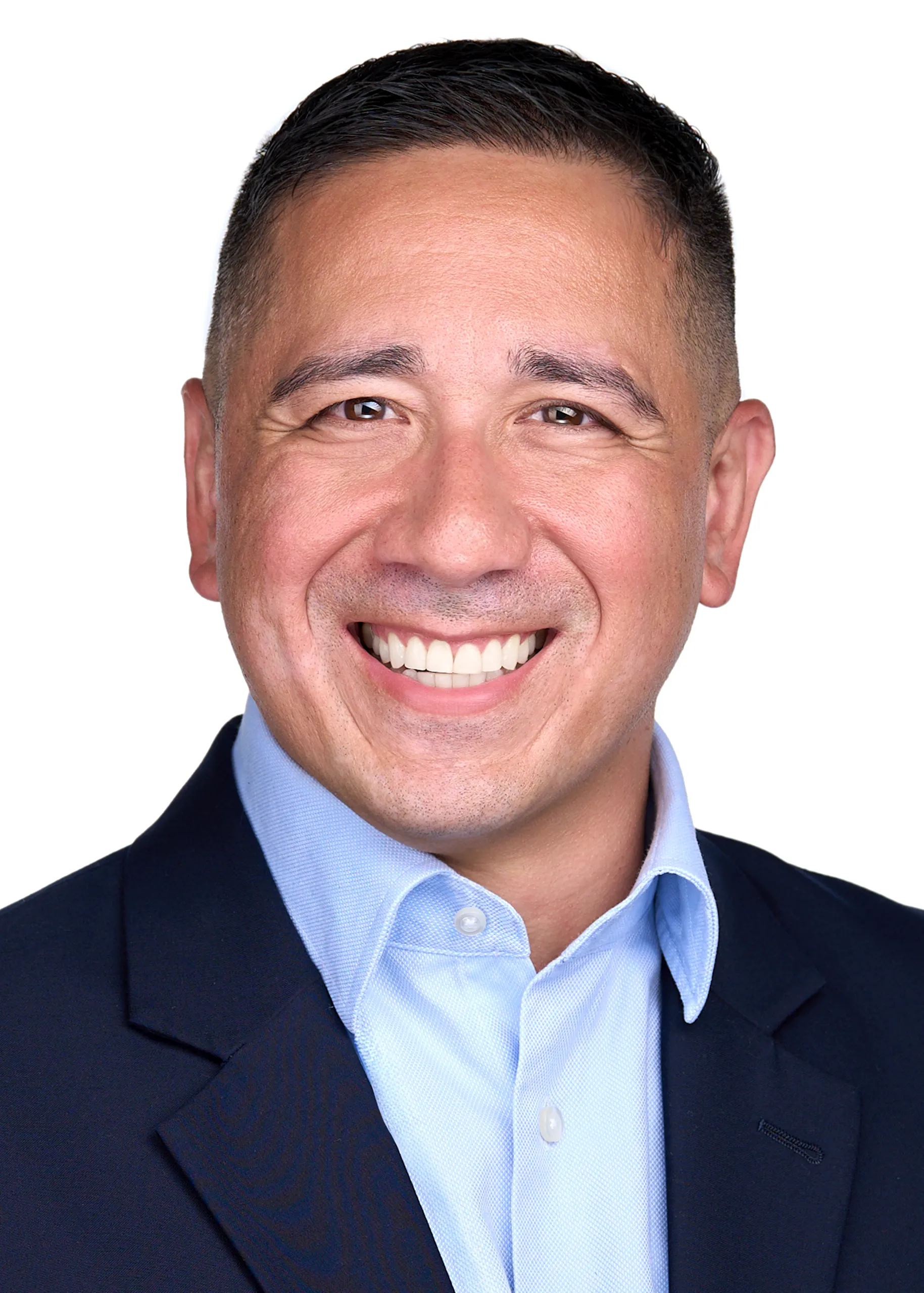 A man wearing a navy suit and light blue shirt, smiles warmly as he poses for a professional headshot for his Linkedin profile in Cary Nc