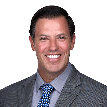 Man in a gray suit jacket, light blue dress shirt, and patterned blue tie, smiling at the camera against a plain white background—an ideal example of professional headshots by a skilled photographer.
