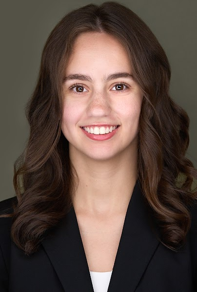 Professional headshot of a smiling woman with long brown hair in a black blazer.