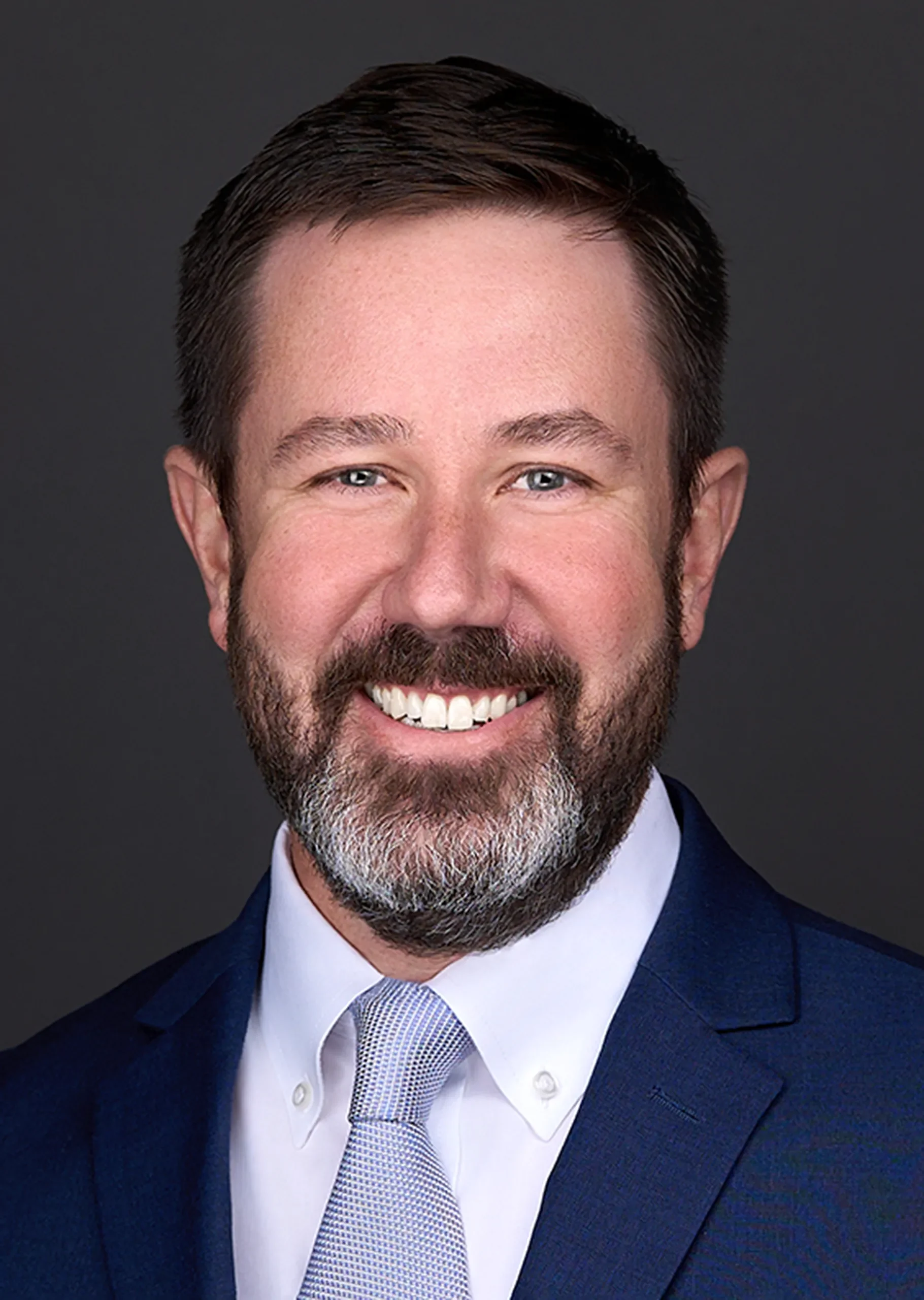 A man with a beard wearing a blue suit and tie sits for a professional headshot in a Cary NC photography studio