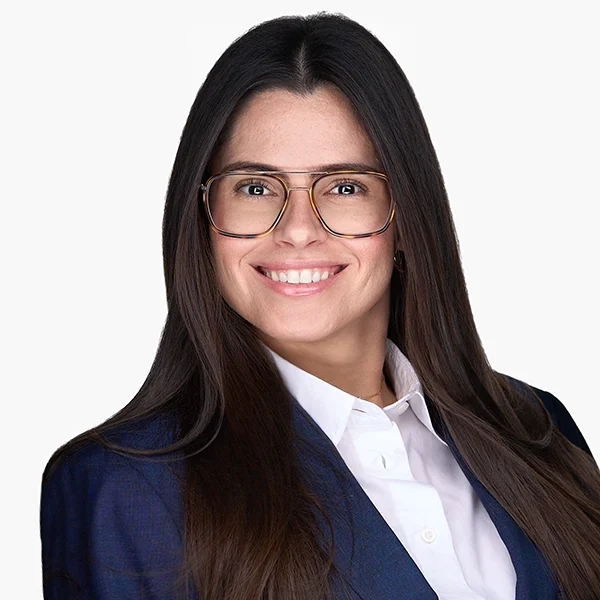 Woman with long brown hair, wearing glasses, a white shirt, and a dark blazer, smiling in a professional headshot against a plain white background. Woman with long brown hair, wearing glasses, a white shirt, and a dark blazer, smiling in a professional headshot against a plain white background.
