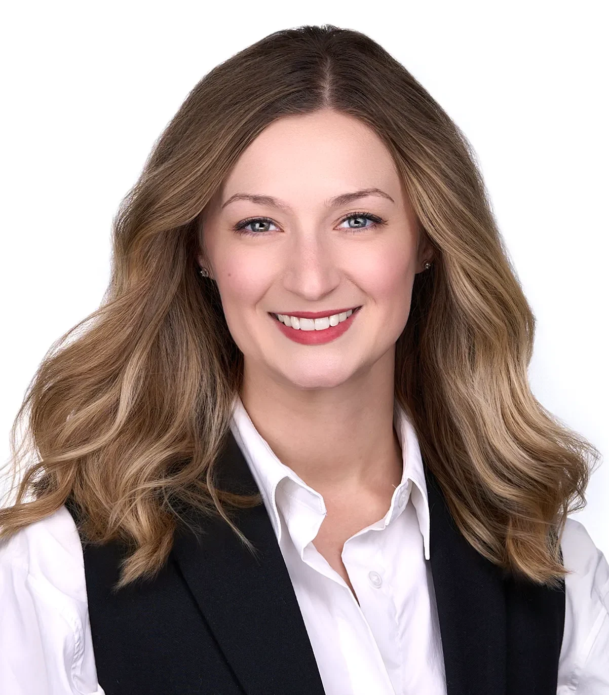 A young woman with long blonde hair is wearinga white button down blouse with a navy vest poses in front of a white backdrop for a professional headshot