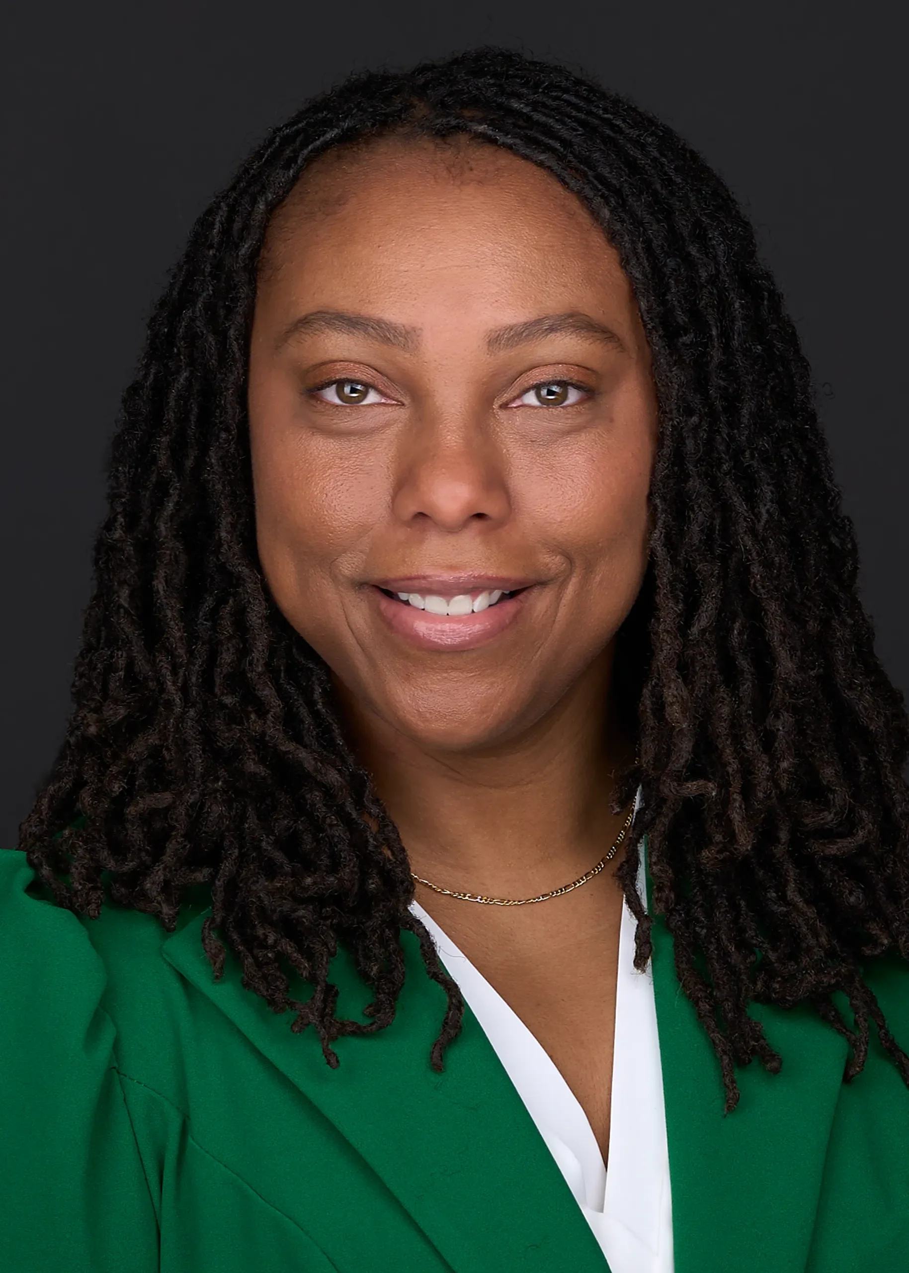 A young woman wearing a green suit is standing in front of a black backdrop as she poses for her Linkedin profile photo in Cary Nc