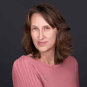 A women sits for a professional headshot wearing a rose colored sweater, posing against a black backdrop.