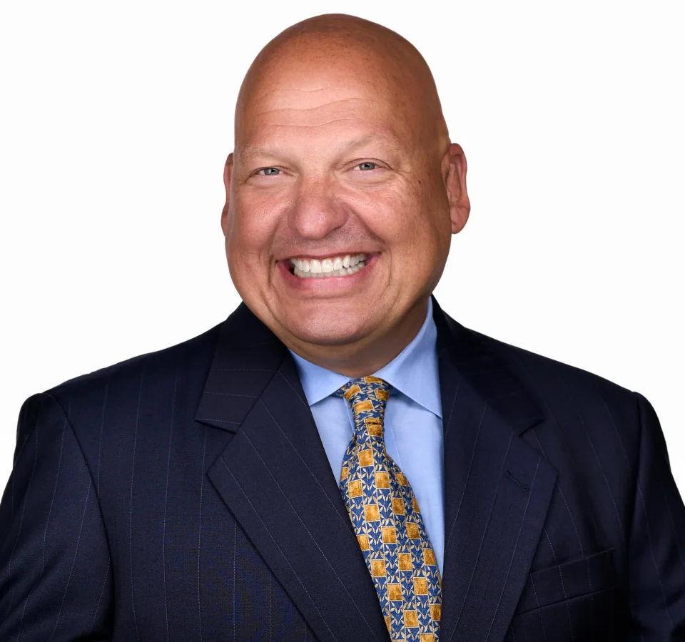 A man wearing a blue suite and yellow tie showcases his warm smile while being photographed for a professional headshot in Raleigh NC