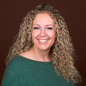 A woman with curly blonde hair wearing a green sweater smiles for the camera in the headshot studio of Sarah Anne Wilson Photography in Raleigh NC