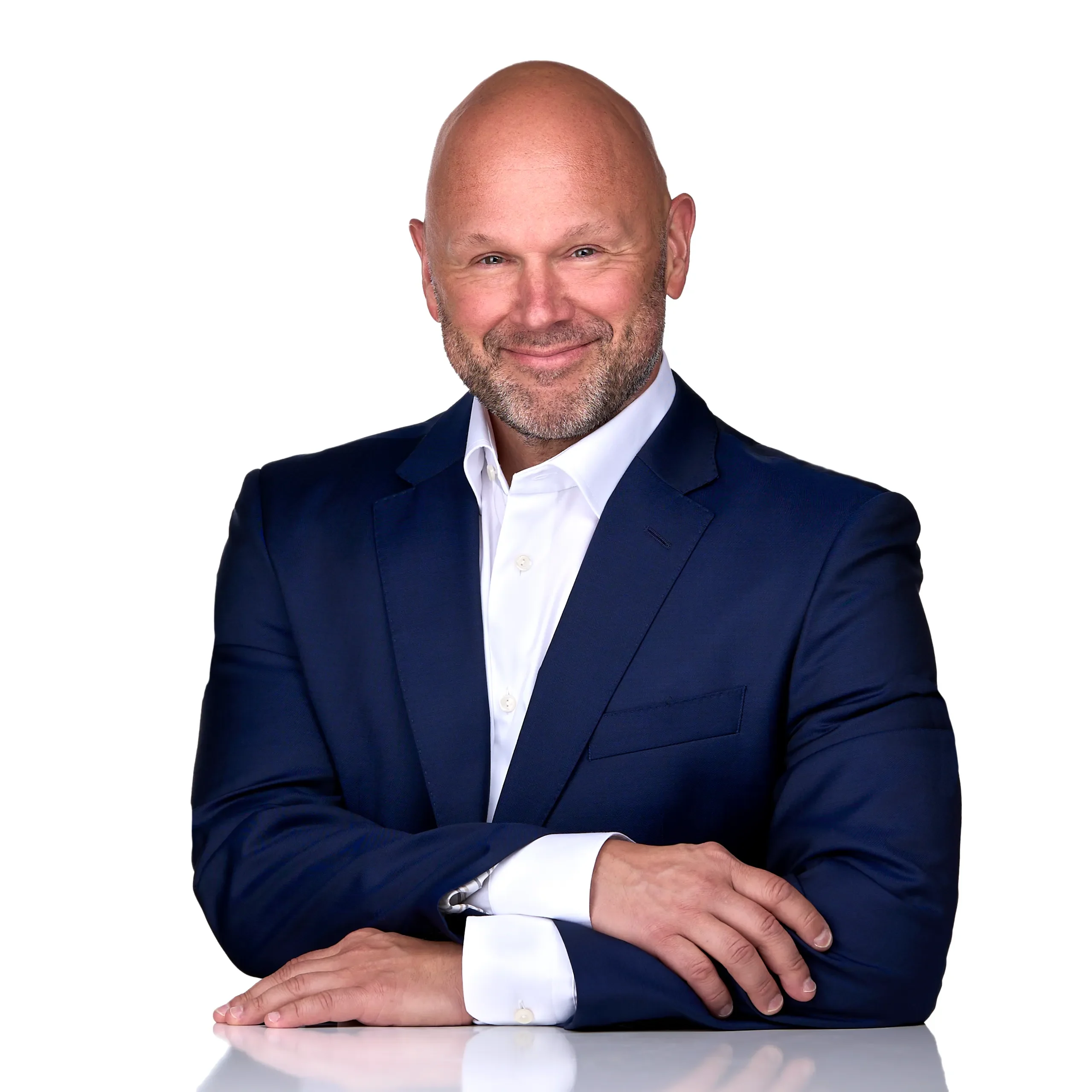 A man wearing a blue suit leans on a white table while he poses for a personal branding headshot in the photography studio of Sarah Anne Wilson in Cary NC