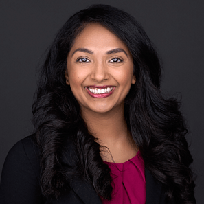 Beautiful young women with long black curly hair wearing a vibrant red top and black blazer sits for a headshot session in Raleigh NC